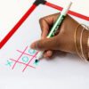 A woman's hand holding a green dry erase marker playing a game of tic-tac-toe on the back of the EZeeCount Abacus.