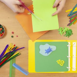 photo shows a pair of hands cutting green paper over a table containing parts from the Tactile and CVI Book Builder kits