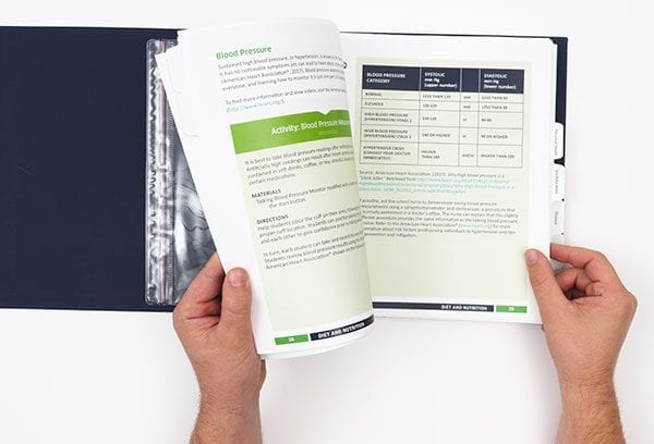 Two hands turning pages of an open blue Health Education guidebook binder.