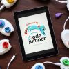 A tablet sitting on a table displaying the Code Jumper logo. Code Jumper pods lay on the table surrounding the tablet.