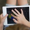 A child outside holding a tablet with an overlay. They are exploring the overlay with their finger.