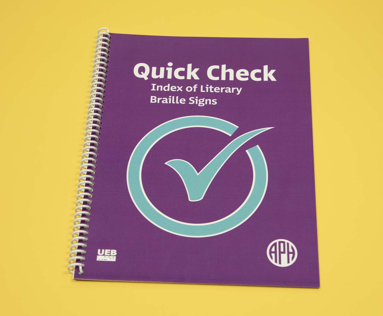 Quick-Check_7-35691-00-web Quick Check Index of Literary Braille Signs Print edition is a spiral-bound book featured over a yellow background. On the purple cover resides a large blue check mark in the middle, a UEB logo in the bottom left-hand corner, and the APH logo in the bottom right-hand corner.