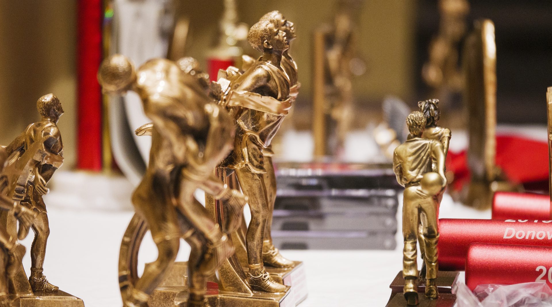 A close up view of several gold athletic trophies and other awards sitting on a table.