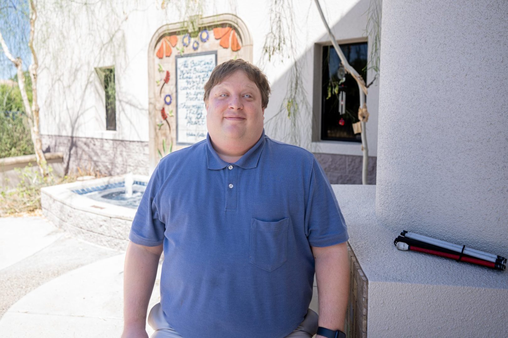 Seth LeBlond poses for a photo outdoors in front of a fountain and beside a column where a folded white cane is resting.