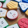Close up of a variety of multicolored UEB Reach & Match number tiles on a wooden surface