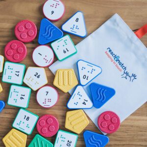 Reach & Match Number Tiles bag filled with multicolored UEB Number Tiles that are spilling out across a wooden surface.