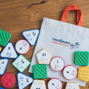 Reach & Match Number Tiles bag filled with multicolored Nemeth Number Tiles that are spilling out across a wooden surface.
