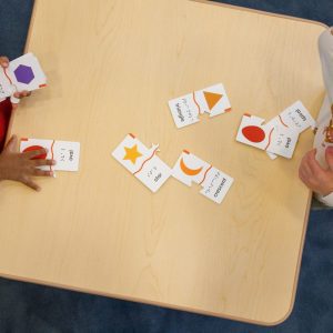 An overhead shot of two preschoolers playing with the Memory Puzzle pieces on a wooden table.