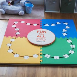 All four pieces of the Reach & Match Light kit assembled in a square on a wooden floor with alphabet tiles inserted into the cut-outs. The carrying case sits in the center and reads "FUN for ALL" with the Reach & Match logo beneath.
