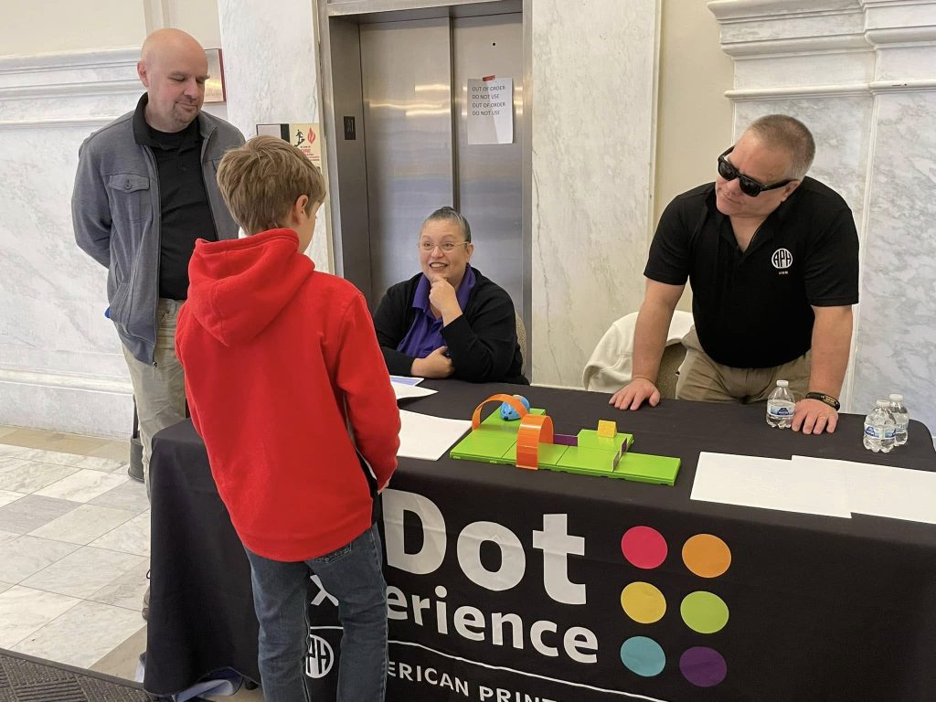 A boy stands in front of a table that reads