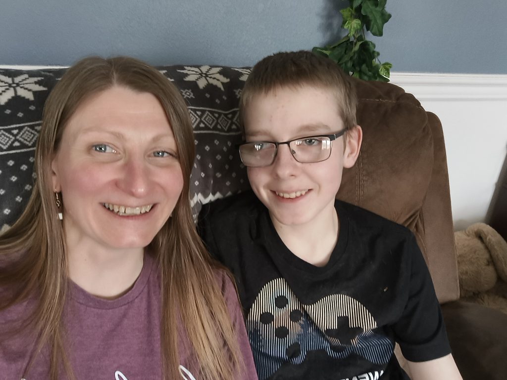 Whitney sits to the right of Ander, who is wearing glasses, as they both smile and look towards the camera.