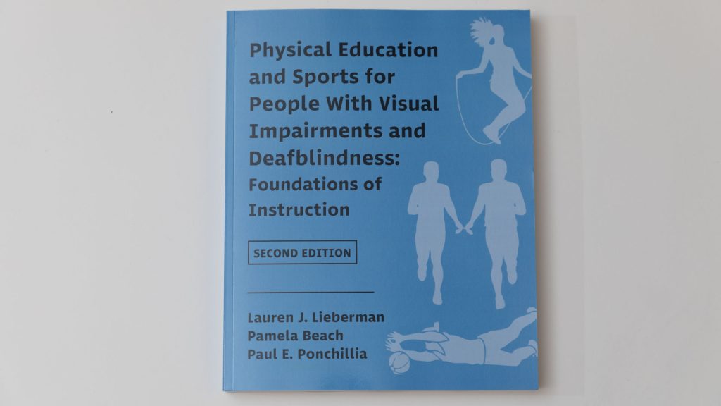 A copy of Physical Education and Sports for People With Visual Impairments and Deafblindness: Foundations of Instruction on a white background. In a lighter blue shade are silhouette figures participating in sports including jump rope and relay racing.