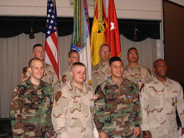 A group of military men at a purple heart ceremony, standing and smiling for a photo in their uniforms. On the bottom left of the group is Tim Hornik.