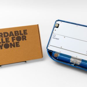 On the right side of the image is a blue Perkins light touch braille writer turned upside down to show the Paige Connect board connected to the base. On the left is the Paige Connect cardboard box that says "Affordable Braille for Everyone."