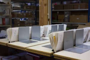 Pages of book text lay inside metal holding spaces, while the glue dries and the printed text waits to be bound. 