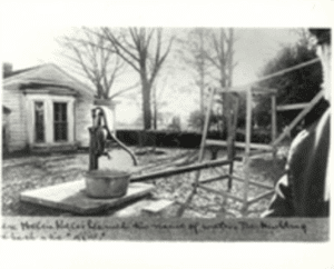 This is an AFB HK Archive photo, and it has been "shopped" with black, grey, and white paint - an extremely common thing to be done to photographs for newspaper and other publications to improve clarity. The 1887 picture shows THE original pump. The 1887 photo is absolutely in the same geographic place in front of the office that the "shed pump" now stands. The picture was taken when Helen was 7 - the photography studio seal and man visible on the side date it well. 