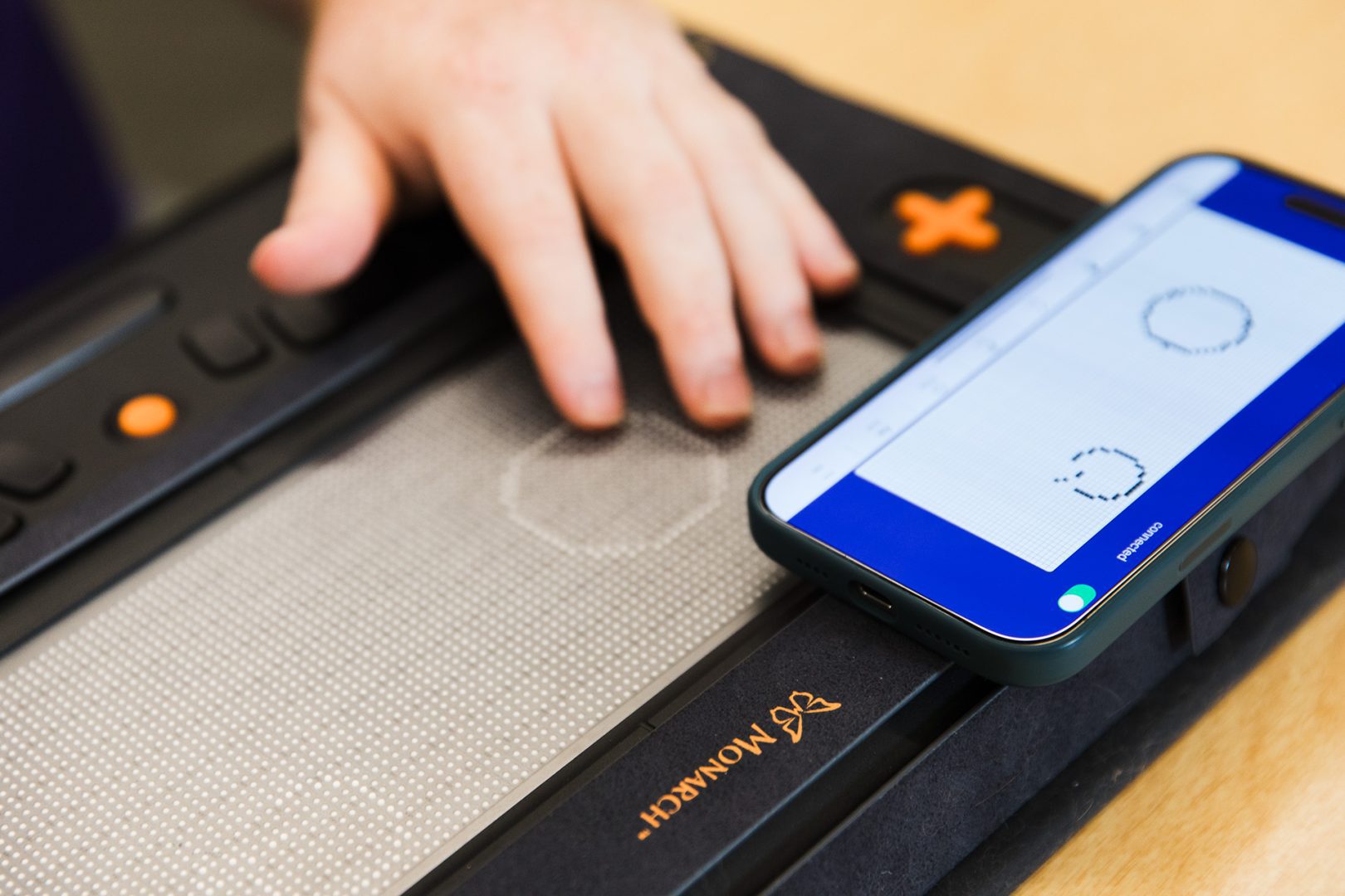 A phone rests on the Monarch with the Wing It app open, showing two drawings. On the Monarch screen below, we see the two shapes in tactile form.