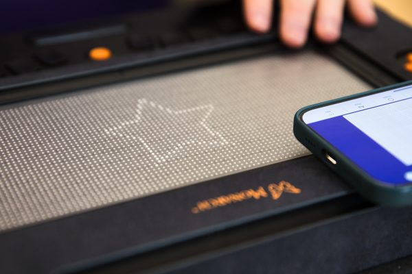 A tactile star graphic displayed on the Monarch. In the corner of the image, an iPhone with the Wing It app open is visible. 