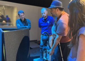 Four adults, one with a cane, stand around the 3-D water pump and feel the exhibit.