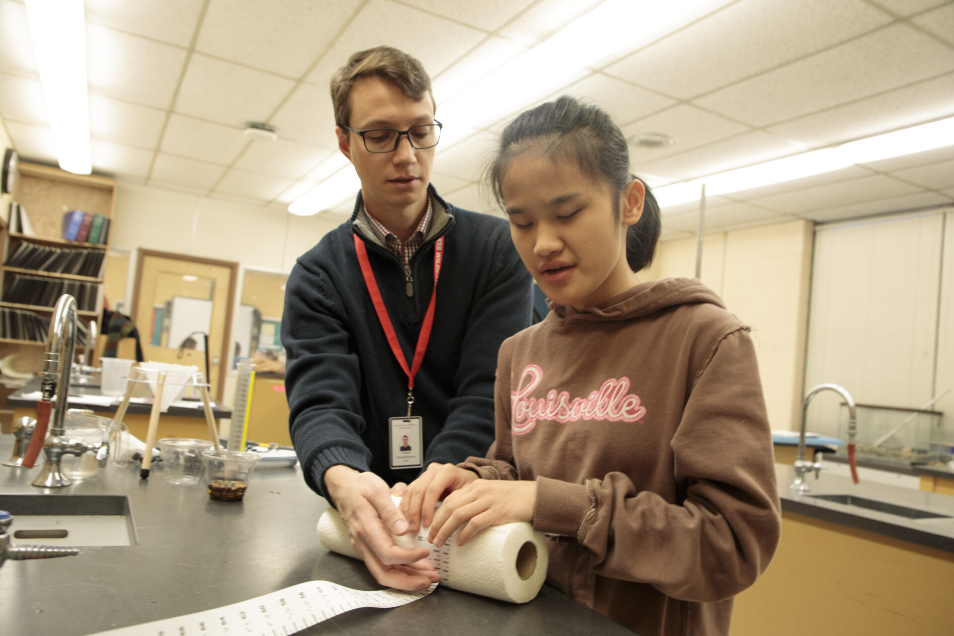 A teacher stands next to a student, who is blind, as he assists her in a science experience using the accessible science kit.