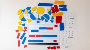 An overhead shot of all the bright red, yellow, and blue fraction pieces as well as the braille labels and white fraction bar tray all laid out on a white background.