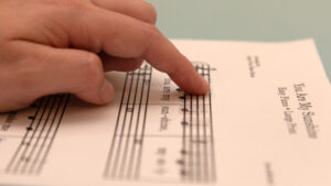 A woman's finger tracing music braille stickers adhered to a piece of printed sheet music.