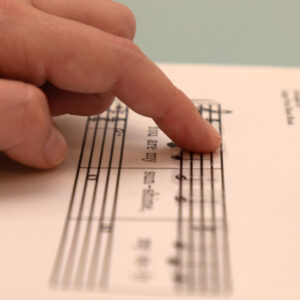A woman's finger tracing music braille stickers adhered to a piece of printed sheet music.
