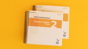 Volumes 1 and 2 of the braille student reader 2 with a yellow stripe across both covers.