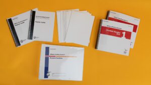 Wilson Reading System IV braille step one on a yellow background, including two volumes of the student reader 1, braille and large print versions of the teacher guide, and the braille student portfolio.