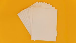A stack of braille sheets stapled into several groups. The sheets have been fanned out and placed on a yellow background.
