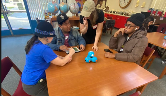 Four adults sit around a table with code jumper modules in the middle of the table.