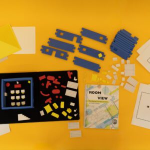 All of the components of the Room With a View kit including tactile graphics, blue foam building block walls, a variety of 3D pieces, and a print guidebook all laid out on a yellow background.