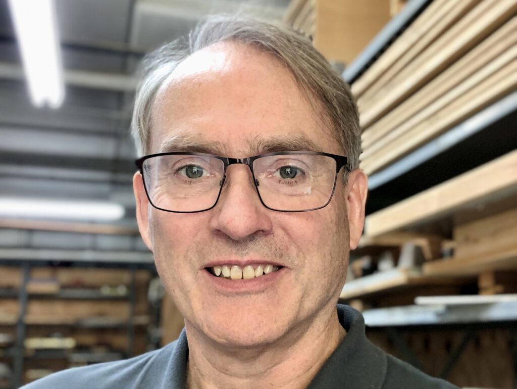 Andrew, a man with brown/grey hair and glasses smiles in a selfie.