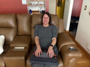 Jennifer sits on a brown couch, while reading on her Monarch that is sitting in her lap.