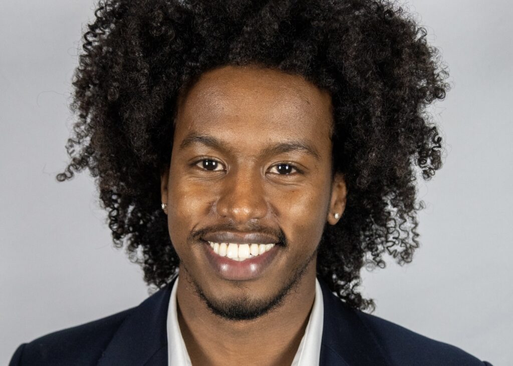 Faid, wearing a black suit, smiles.