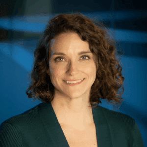 Stacy Branham dressed in green with a blue backdrop. She has chin-length hair and is smiling at the camera.