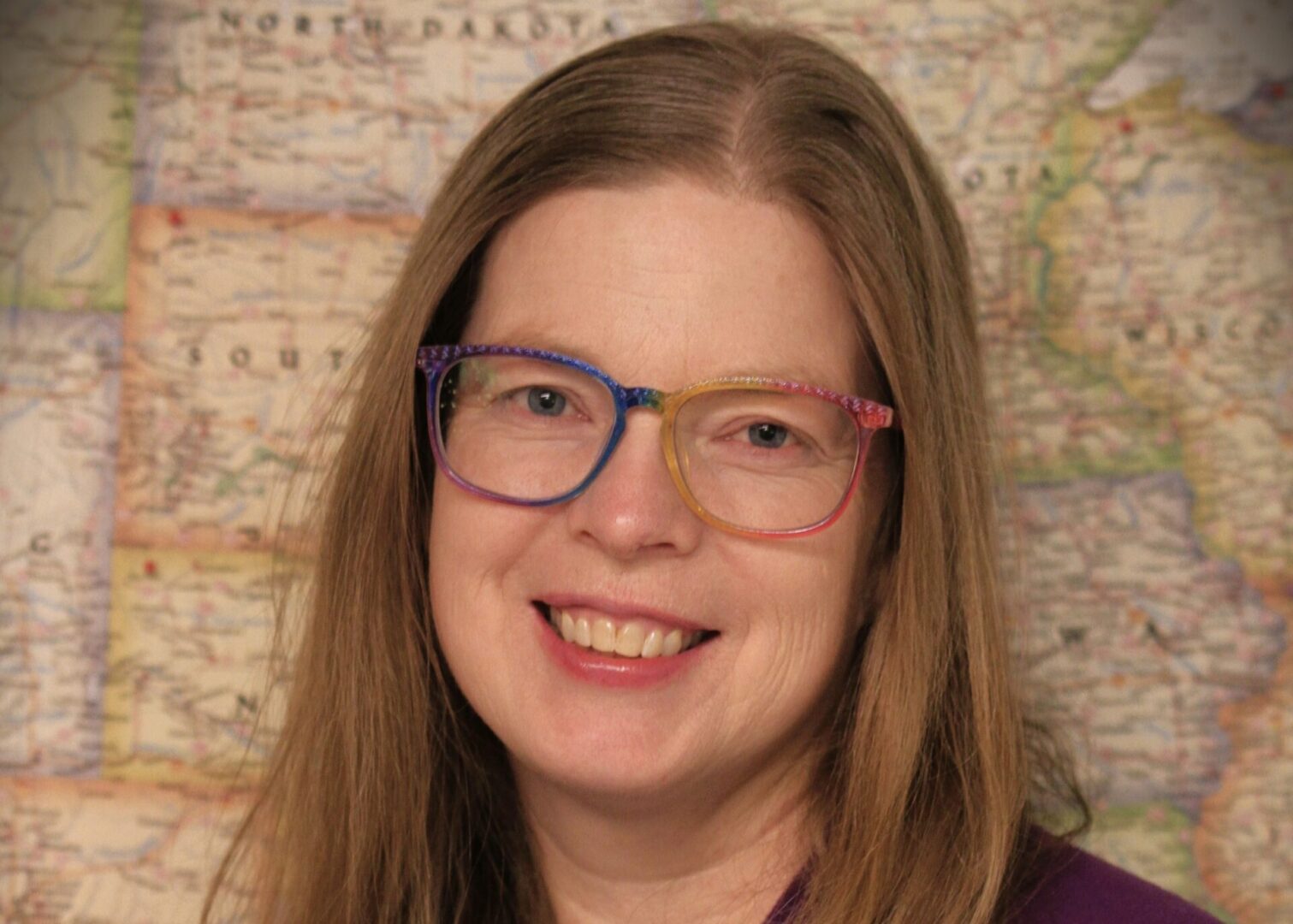 Anita, wearing colorful glasses, smiles in front of a map backdrop.