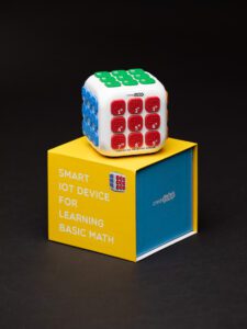 Creacube with the red buttons facing forward sitting on top of the yellow and blue box.