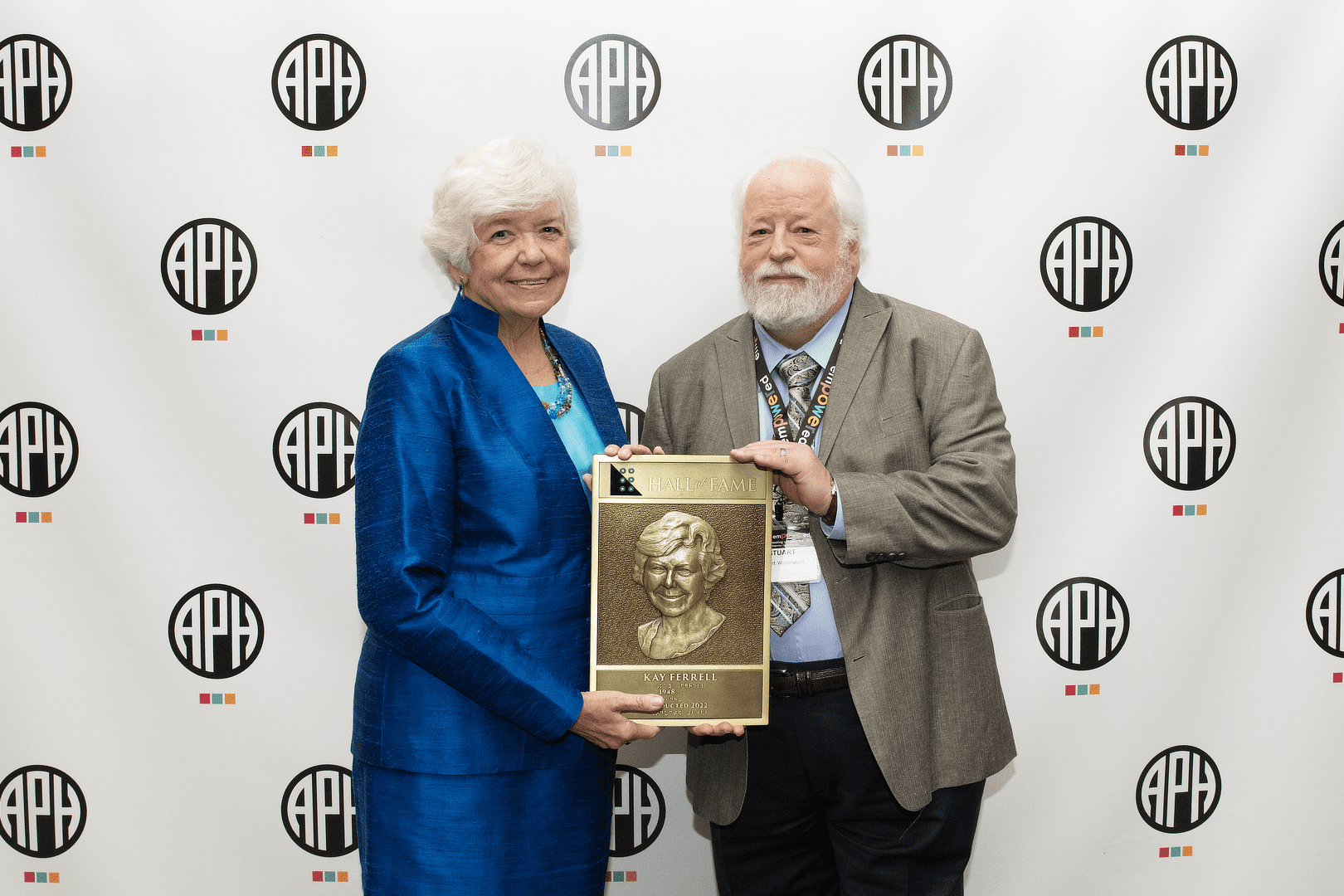 Kay A. Ferrell accepts the Hall of Fame award. She is dressed in a blue suit and stands next to a gentleman with a white beard wearing a light-colored suit.
