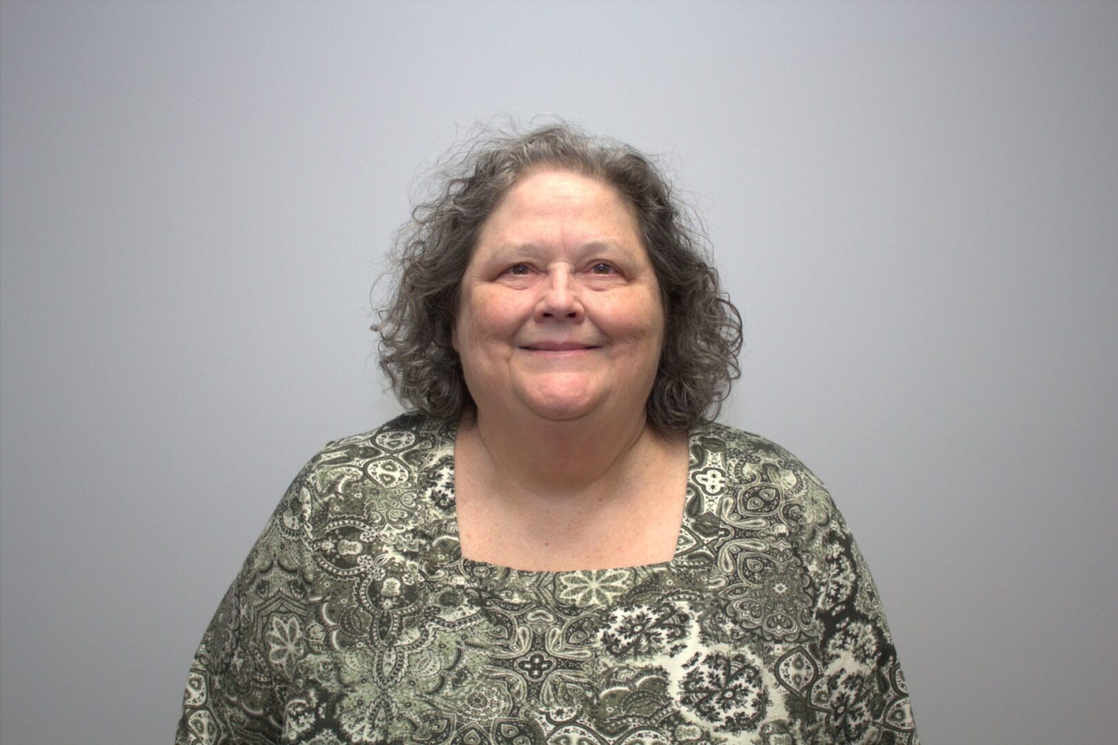 Jo Holt, wearing a floral green shirt, stands in front of a plain background smiling at the camera.