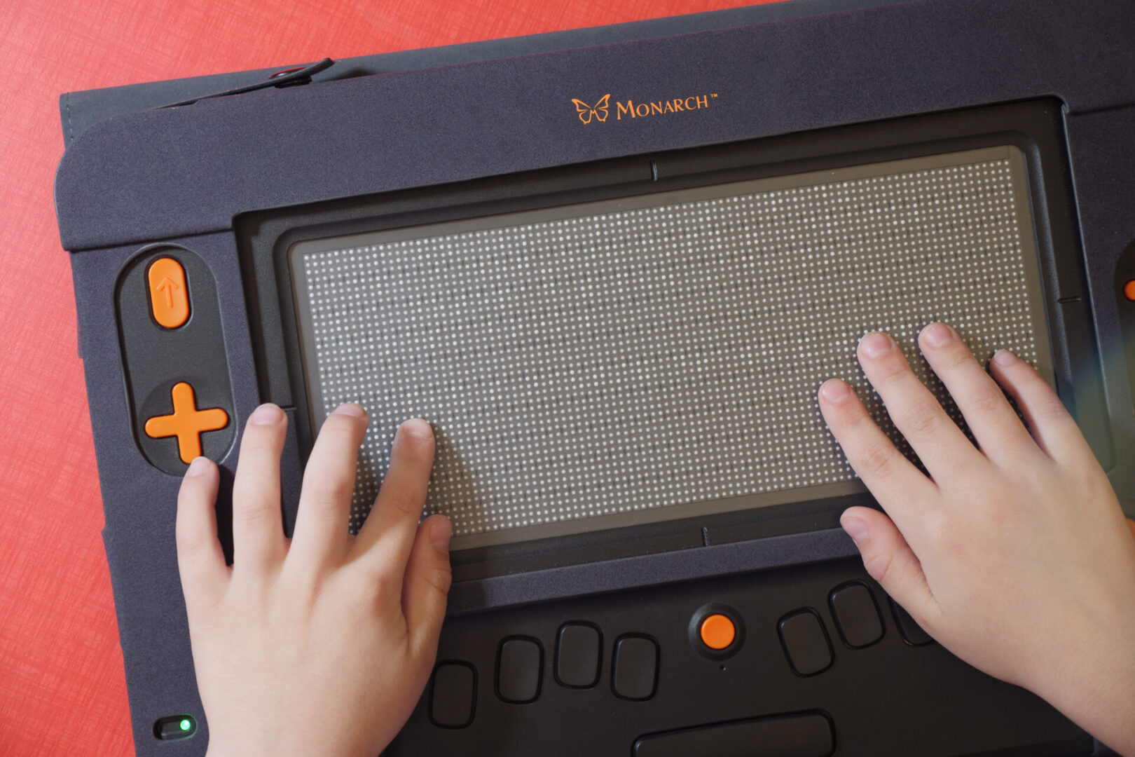 Two hands sit on the Monarch, reading through lines of braille text.