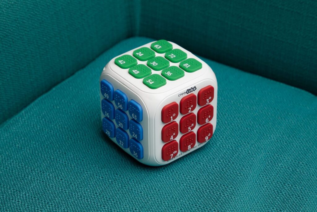 Creacube with the red buttons facing forward sitting on top of the yellow and blue box.