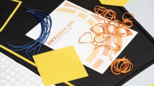 A close-up of the AnyMath Kit print teacher's guide with blue and orange cord arranged on the cover. A square manipulative is placed in the bottom left corner.
