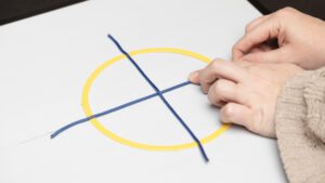 A hand exploring a tactile yellow circle placed on an AnyMath board with blue line strips dividing the circle into fourths.