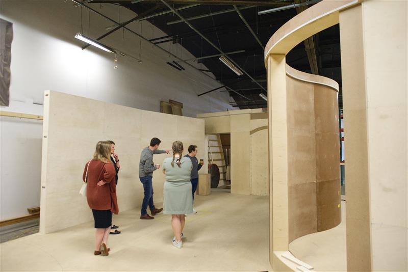 A group of people walk around a wooden model of The Dot Experience Museum