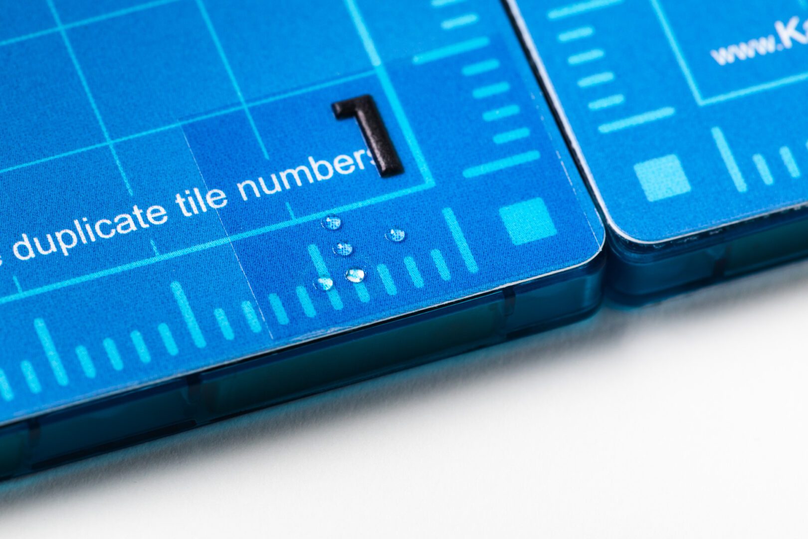 A close-up of two KaiBot magnetic tiles joined together. A braille number is in the corner.