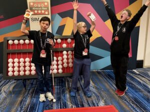 Three students wearing medals celebrate in front of a giant abacus.